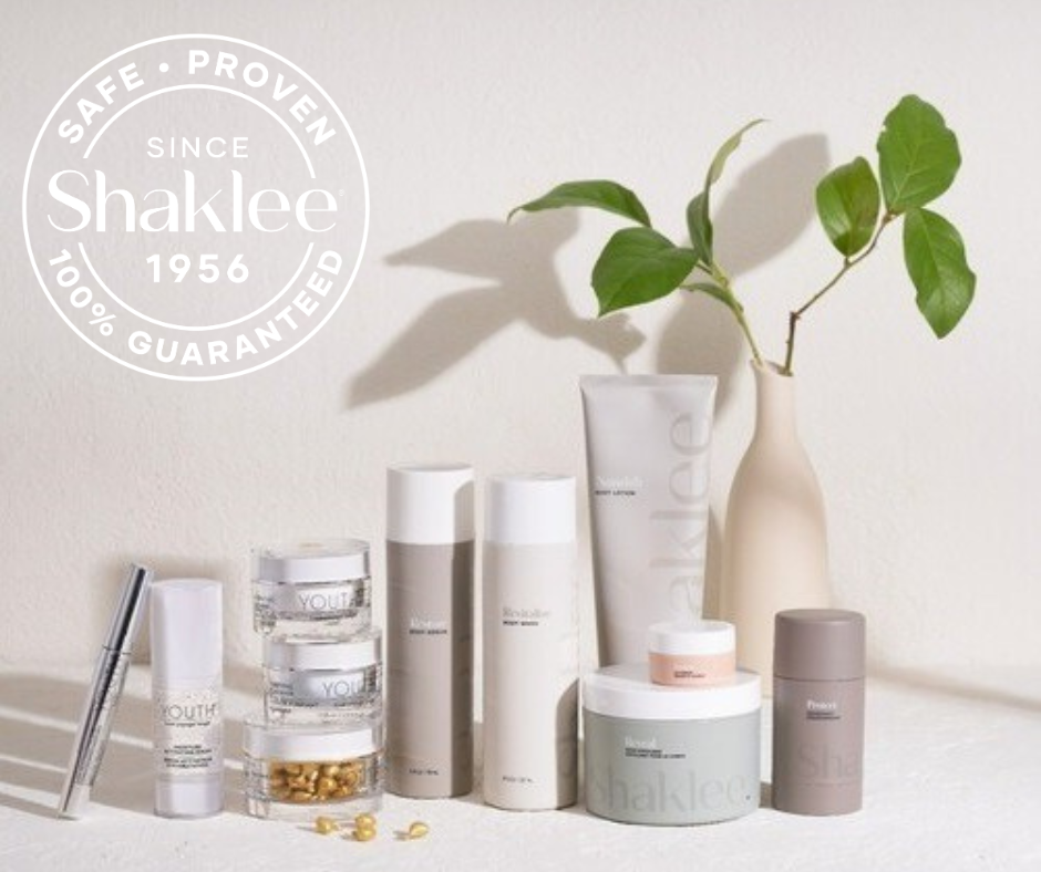 Assorted Shaklee skincare products on a white surface with a pale vase and plant; circular Shaklee logo watermark upper left.