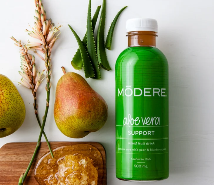 Modere Aloe Vera Australia Gut Tonic - Image 4 - Shop Shaklee Australia Green Modere aloe vera drink bottle with pears, aloe leaves, and honey on a cutting board — natural ingredients highlight the product theme.