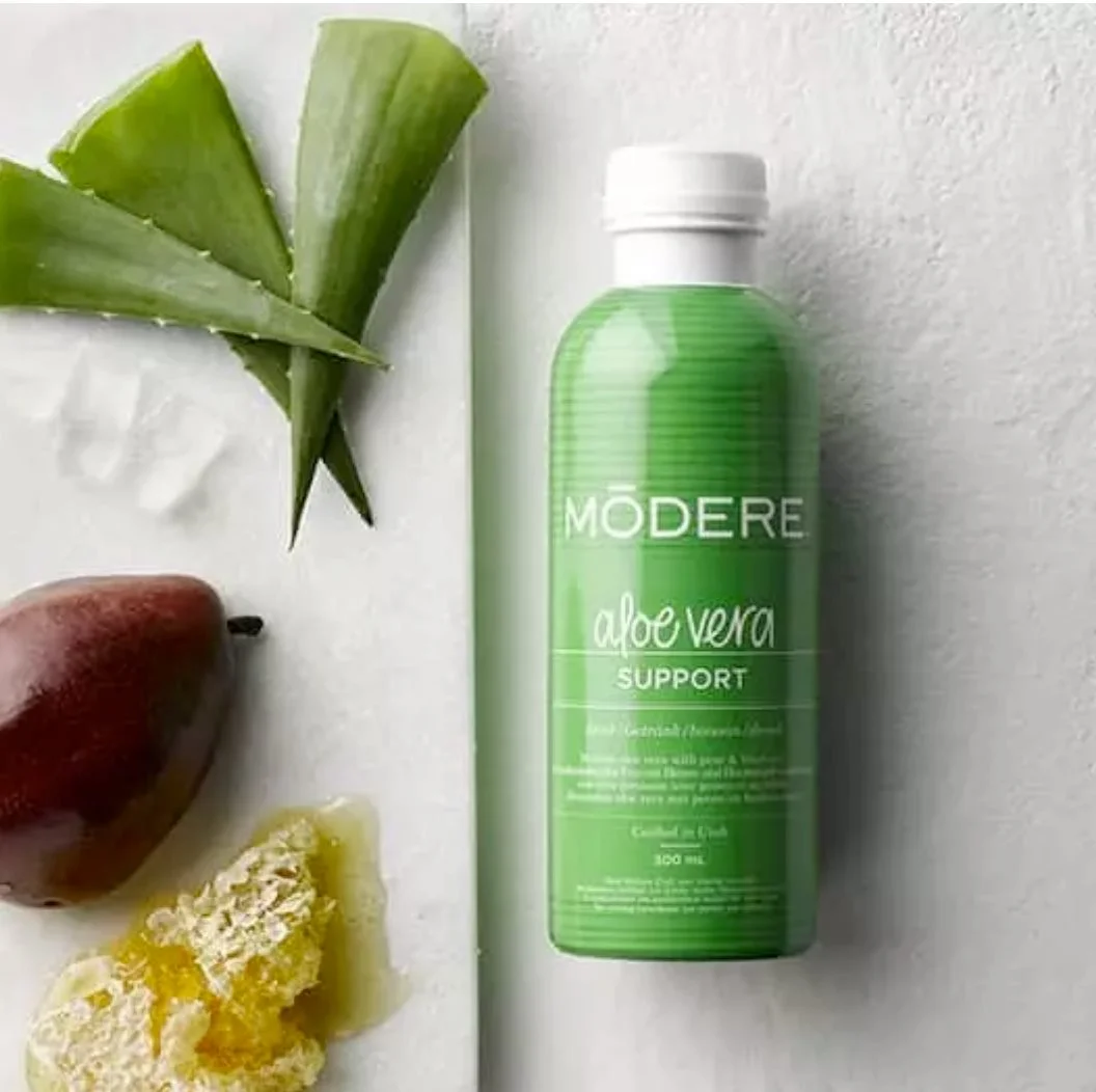 Modere Aloe Vera Australia Gut Tonic - Image 2 - Shop Shaklee Australia Green Modere Aloe Vera Support bottle on a light surface with fresh aloe leaves nearby and fruit pieces (for context: aloe vera supplement).