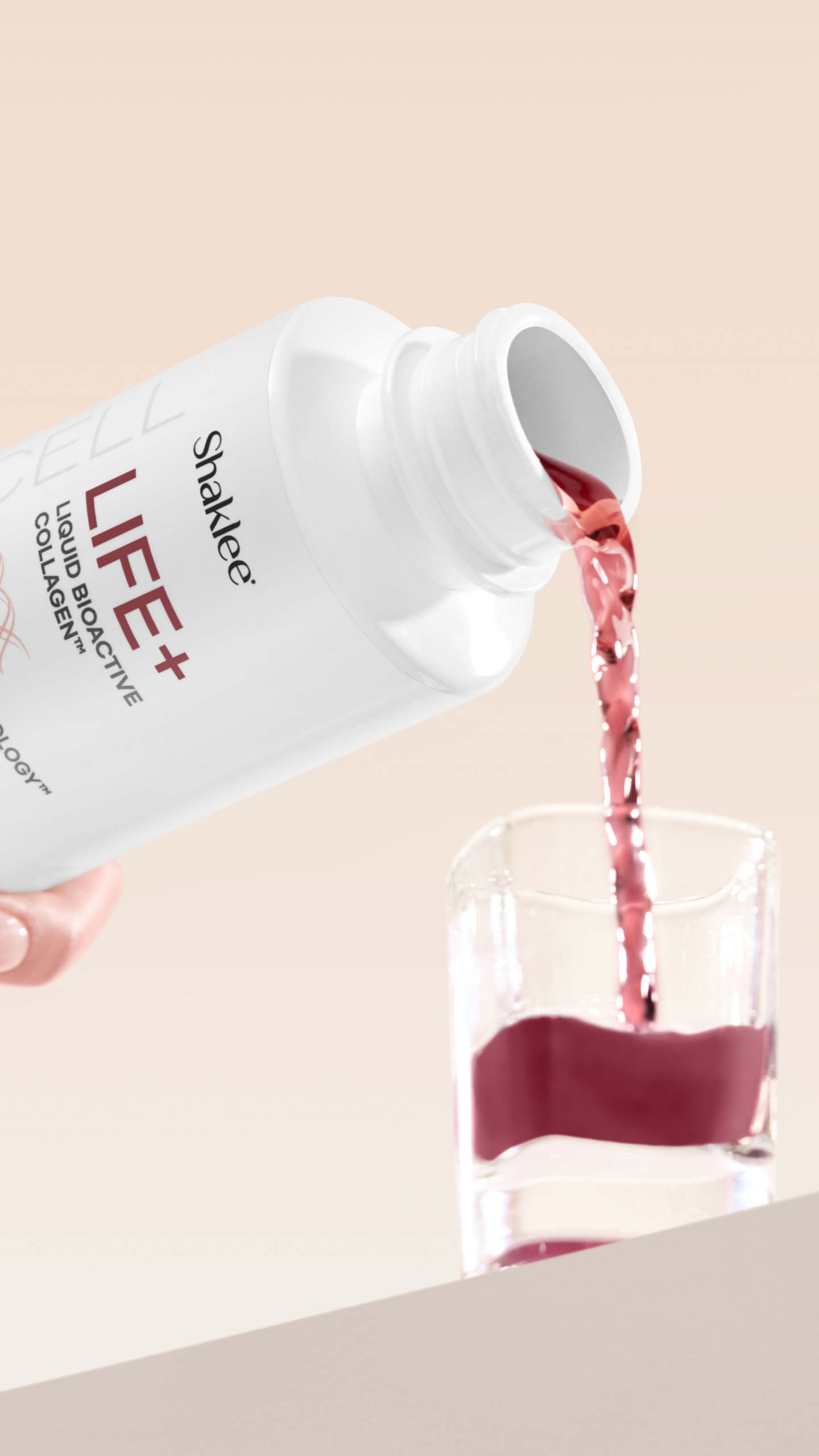 Life Plus Bottle Pour in Glass Story on Peach Background - Shop Shaklee Australia White LIFE+ supplement bottle pours pink liquid into a glass, close-up shot.